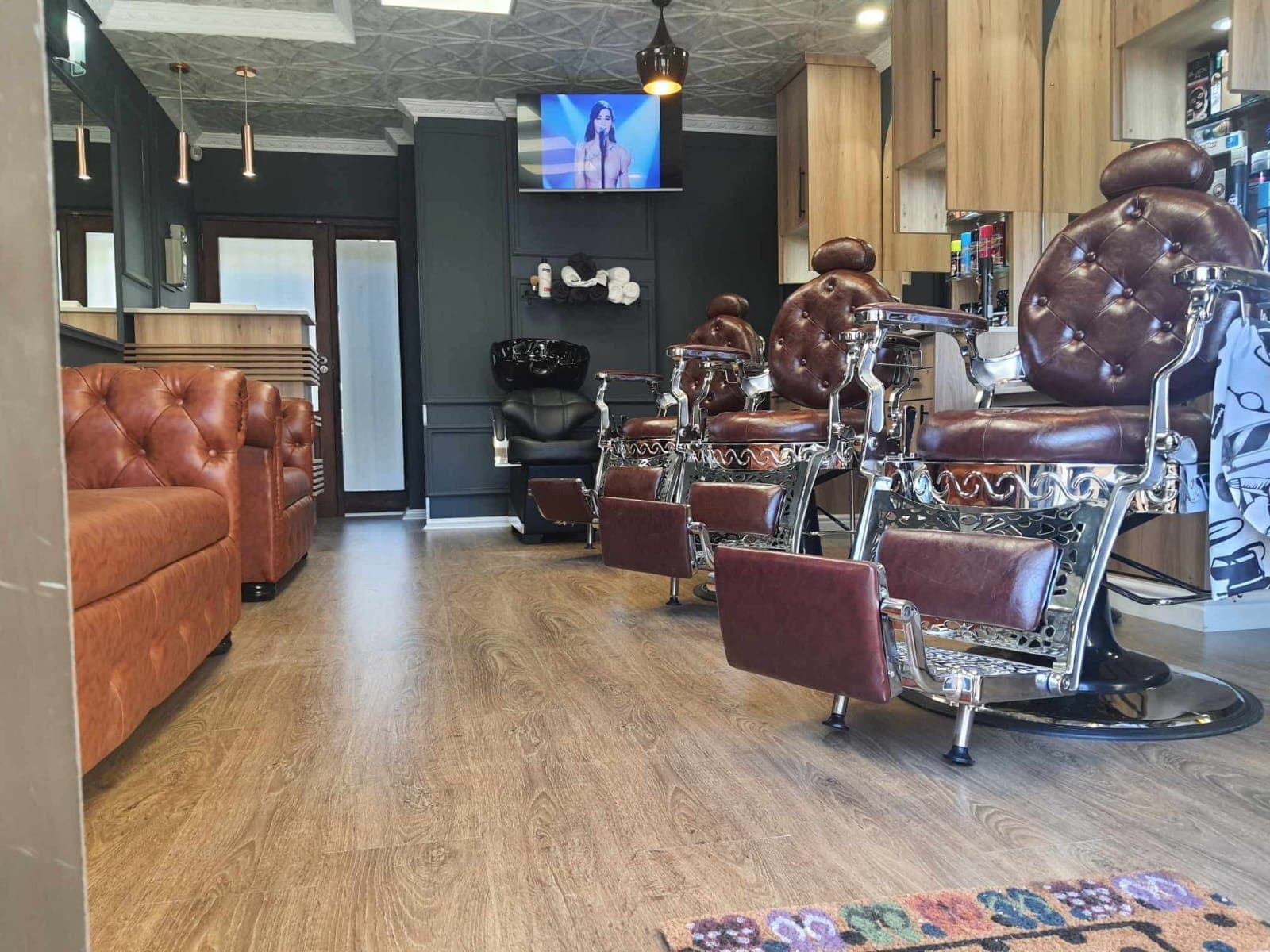 Upscale barbershop interior with vintage tufted leather chairs, a tan sofa, and dark walls.