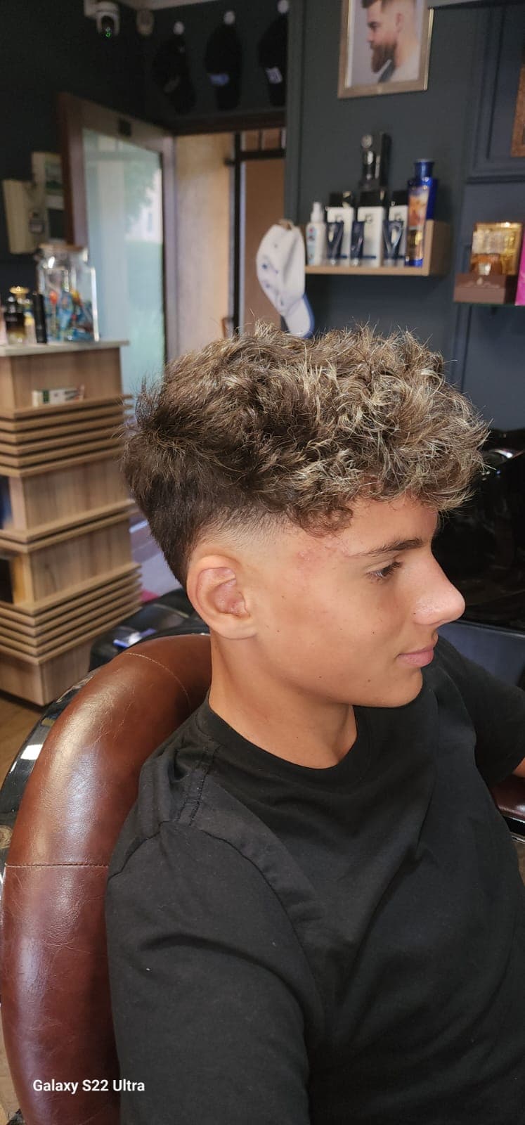Young man with curly highlighted hair and a skin fade haircut in a barbershop.