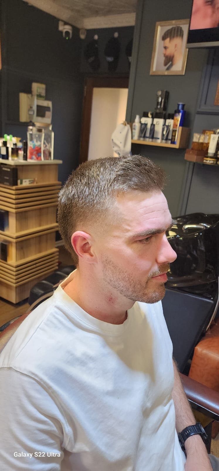 Man with a short, faded haircut and trimmed beard sitting in a barbershop chair.