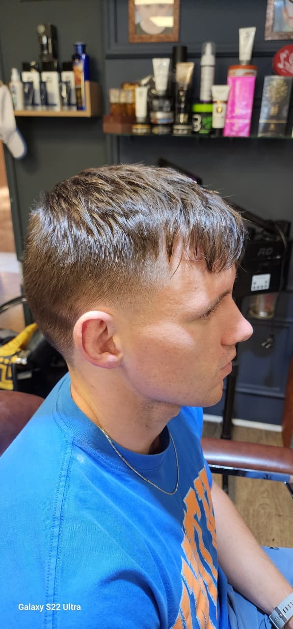Man with a short textured haircut and faded sides sitting in a barbershop chair.