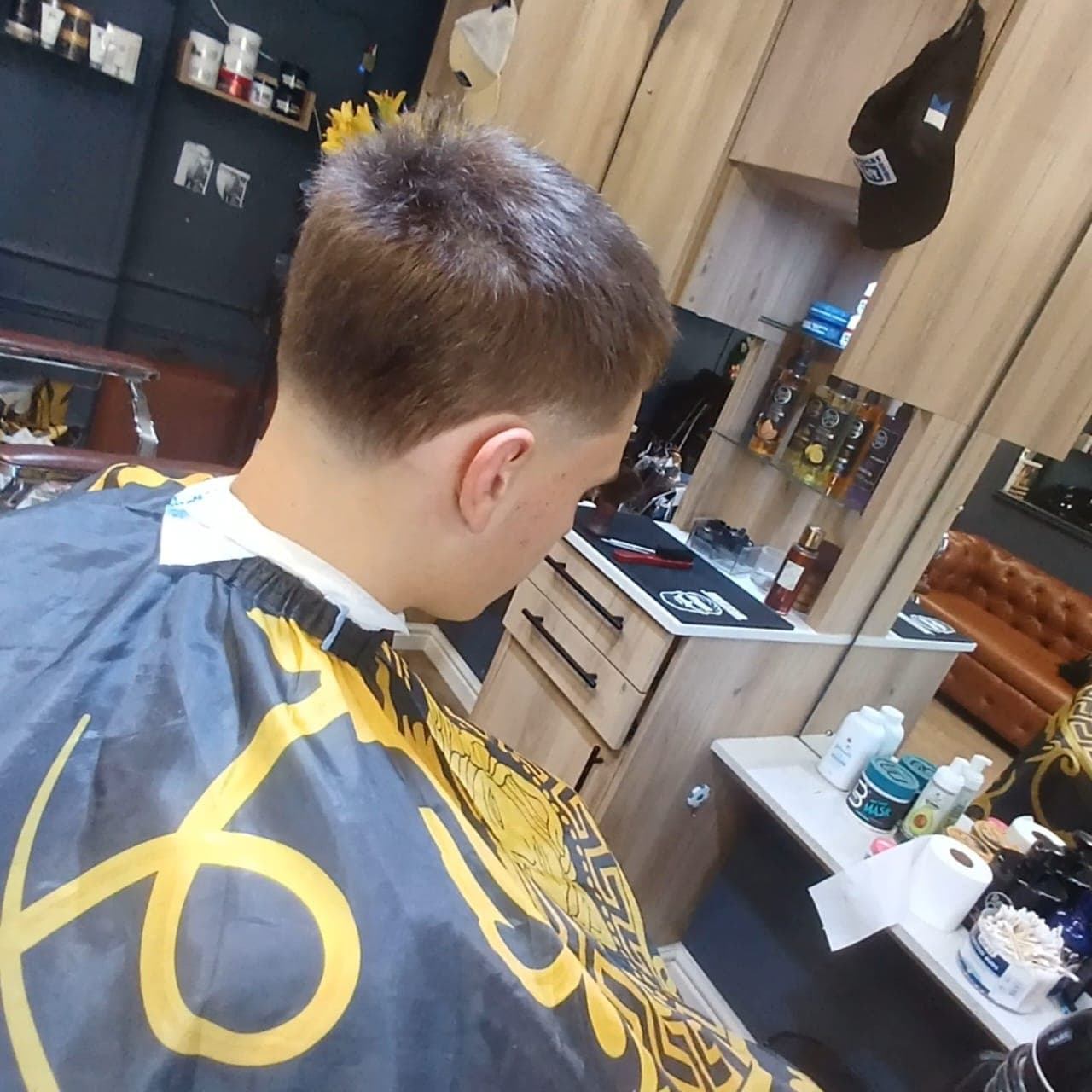 Young man with a fresh taper fade haircut sitting in a barbershop wearing a cape.