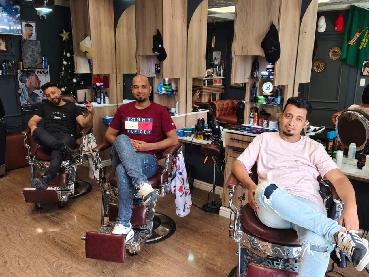 Three men sitting in vintage-style barber chairs inside a modern barbershop with wooden decor.